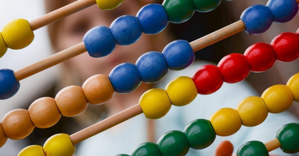 Close-up of colorful wooden abacus with a child learning math in the background, focusing on education and early childhood development.