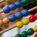 Close-up of colorful wooden abacus with a child learning math in the background, focusing on education and early childhood development.