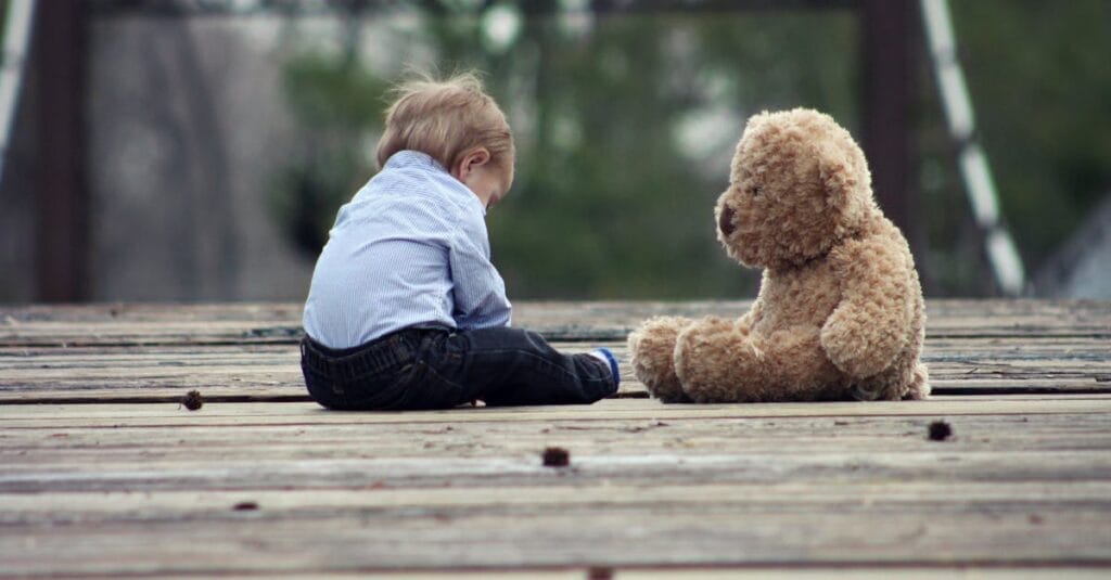 Adorable toddler sitting with a teddy bear on a wooden bridge, enjoying a peaceful moment outdoors.