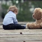 Adorable toddler sitting with a teddy bear on a wooden bridge, enjoying a peaceful moment outdoors.