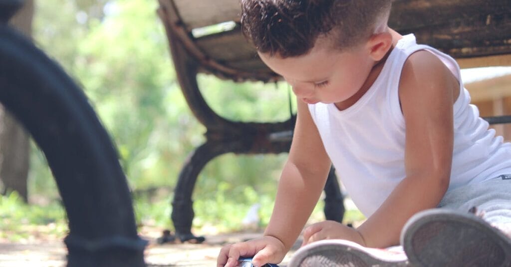 A young boy engaged in imaginative play with a toy car in a sunny park setting.