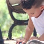 A young boy engaged in imaginative play with a toy car in a sunny park setting.