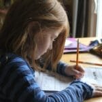 Young girl focused on homework at kitchen table with natural light.