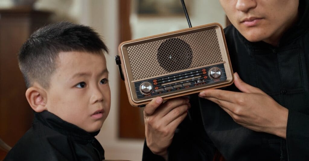 Father and son sharing a moment, listening to a vintage transistor radio indoors.