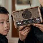 Father and son sharing a moment, listening to a vintage transistor radio indoors.