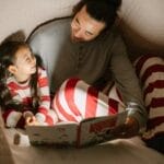 Father and daughter enjoy a bedtime story under a cozy blanket, sharing smiles and bonding.