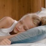 A young girl peacefully sleeping in a comfortable bed amidst soft pillows and blankets, evoking tranquility.