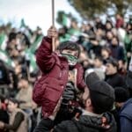 Crowd gathers in Idlib, Syria for a protest, featuring a child with a flag.