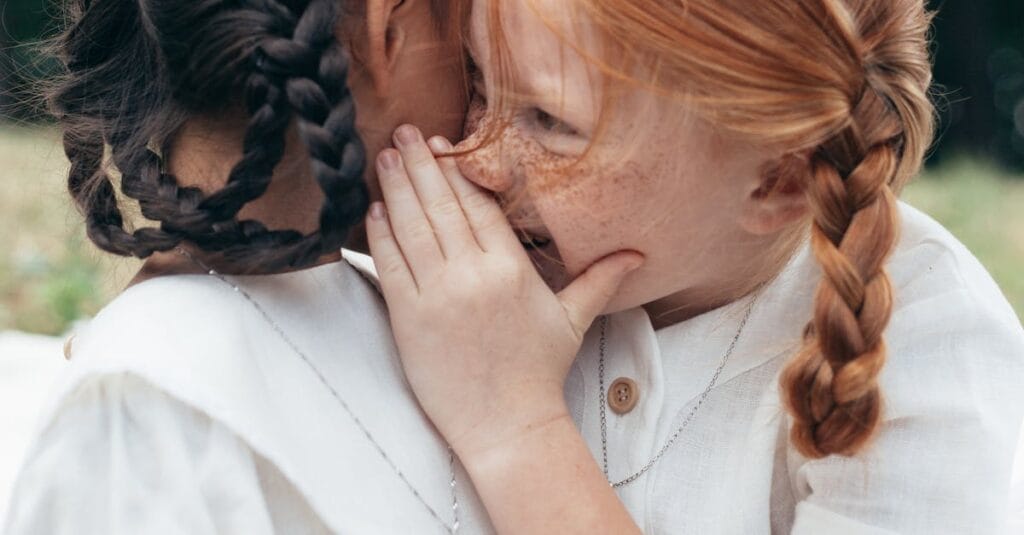 Two children whisper a secret, showcasing friendship and innocence outdoors on a bright day.