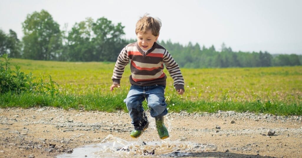 A cheerful child in a striped sweater jumps into a puddle on a sunny day in Czechia.