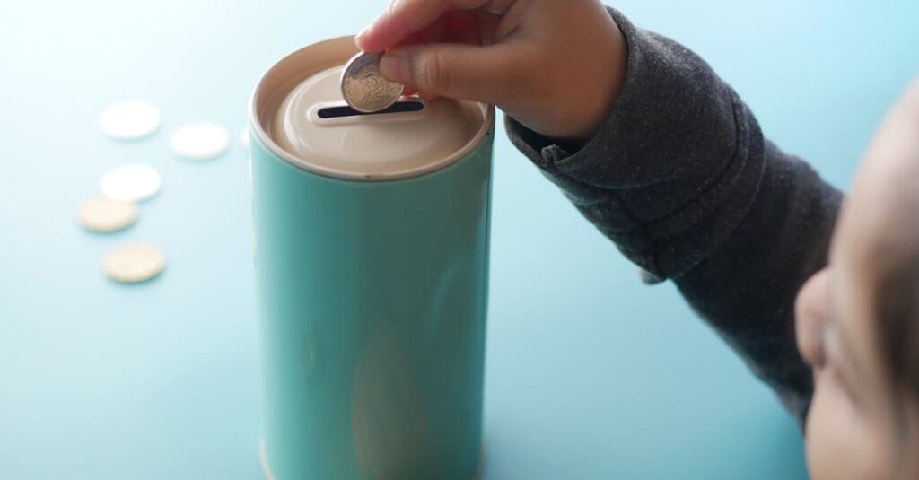 A child placing a coin into a teal piggy bank, representing saving money and financial education.
