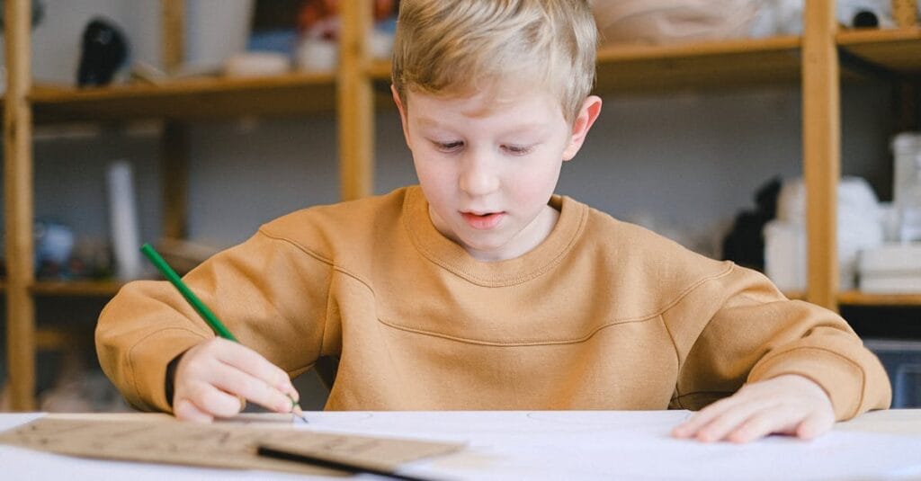 A young boy in a cozy setting focused on drawing with colored pencils.