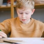 A young boy in a cozy setting focused on drawing with colored pencils.