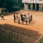 Group of children playing together on a sunny day in a school yard with murals outside.