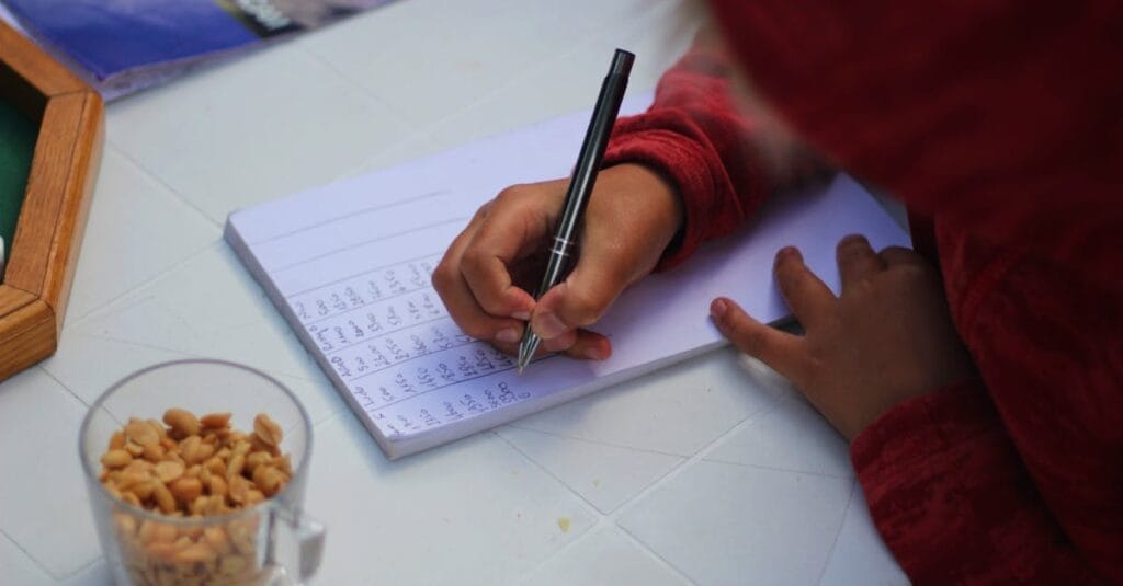 A child writing notes outdoors with peanuts on the table, showcasing focus and concentration.