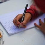 A child writing notes outdoors with peanuts on the table, showcasing focus and concentration.