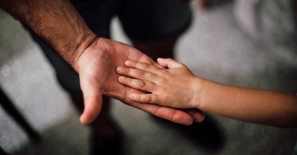 Close-up of a child's hand resting gently on a man's hand, symbolizing love and support.