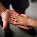 Close-up of a child's hand resting gently on a man's hand, symbolizing love and support.