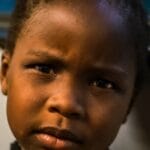 Close-up portrait of an African American girl with a thoughtful expression, captured indoors.