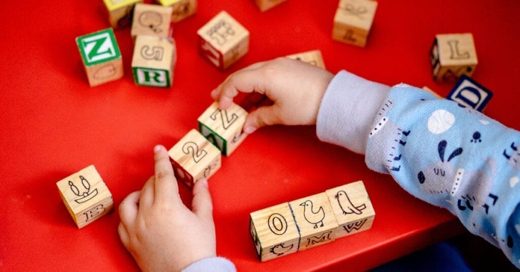 Young child engaging with wooden alphabet blocks on a vibrant red table, learning and playing.