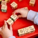 Young child engaging with wooden alphabet blocks on a vibrant red table, learning and playing.