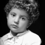 Artistic black and white portrait of a young child with curly hair, wearing a white shirt.