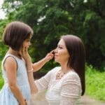 A loving interaction between a mother and daughter surrounded by lush greenery, showcasing a beautiful bond.