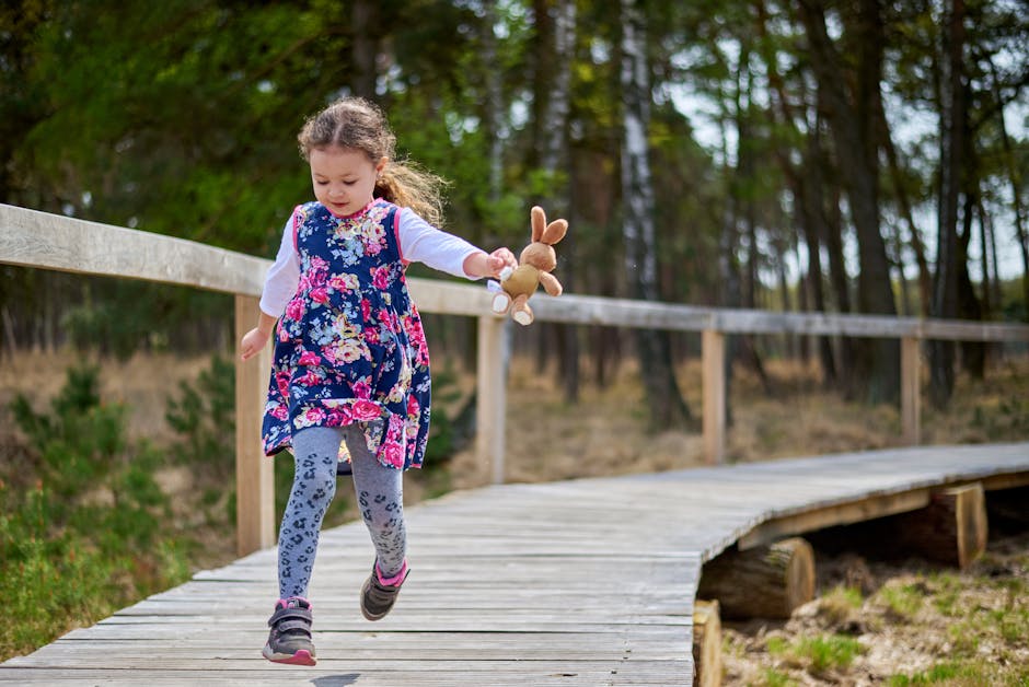 Young girl in a floral dress runs with toy rabbit on a forest boardwalk, embracing nature.