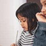 Two young girls joyfully engaged in creative learning indoors, capturing a candid moment of togetherness.