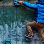 Young boy in blue jacket climbing a painted rock wall outdoors, showcasing adventure and play.