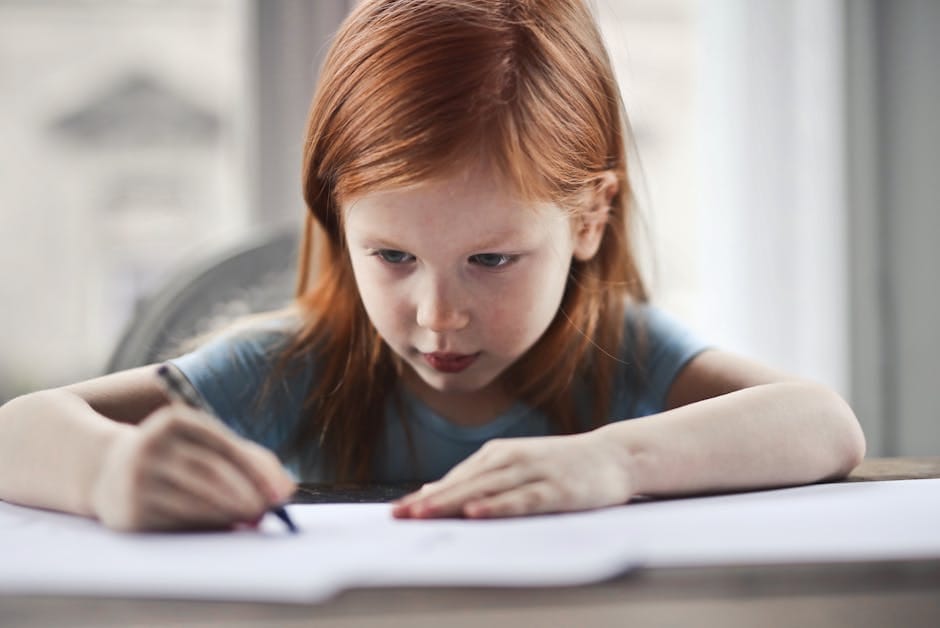 Focused young girl with red hair writing on paper at a desk indoors.