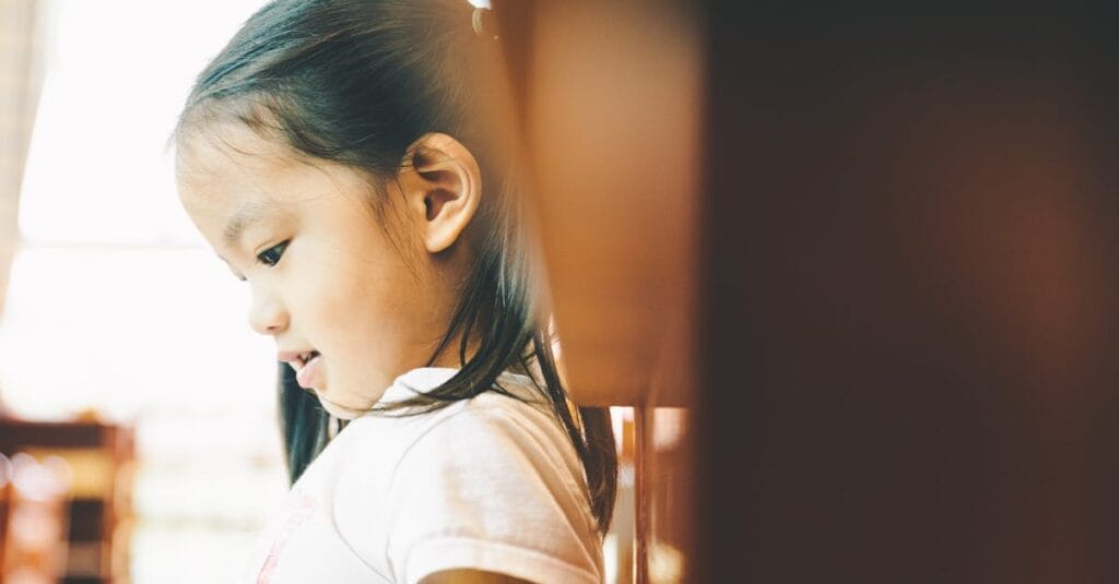 A serene portrait of a young girl in profile, thoughtfully looking down in a warmly lit indoor setting.