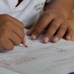 Close-up of a student writing math equations in a notebook with a pencil indoors.