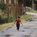 A young boy runs joyfully on a rustic street in São Paulo, holding a paper plane.