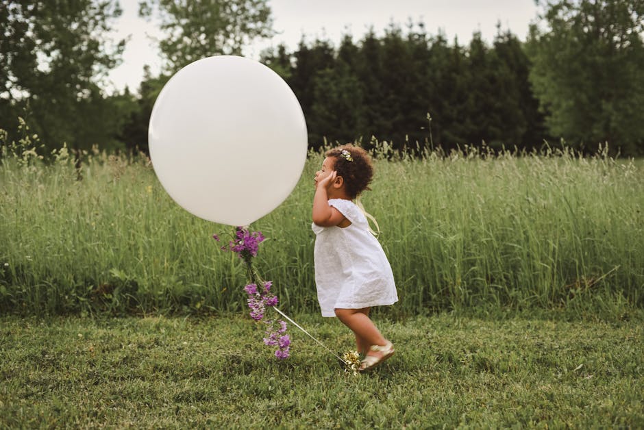 A happy child enjoying a large white balloon in a lush green field.