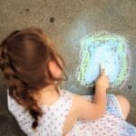 A young girl creatively drawing on the sidewalk with colorful chalk, capturing a moment of childhood creativity.