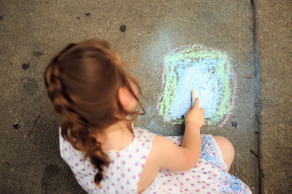 A young girl creatively drawing on the sidewalk with colorful chalk, capturing a moment of childhood creativity.