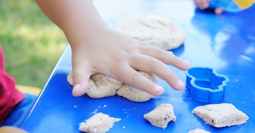 Young child having fun playing with colorful clay at an outdoor table.