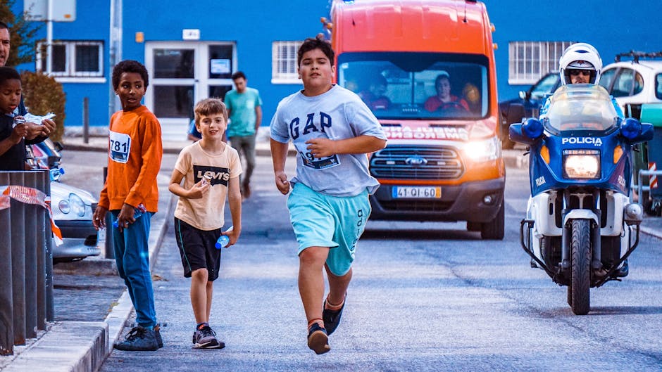 Children running in an urban setting with police motorcycle escort and emergency vehicles present.