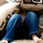 A child crouched under cushions on a couch, conveying a sense of playfulness or fear.