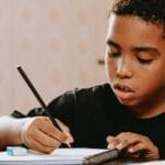 A young boy intensely focuses on writing in his notebook, showcasing educational dedication.