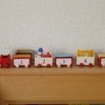 Red and white wooden toy train with numbers displayed on a wooden shelf.