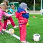 Kids having fun playing soccer outdoors on a sunny day in a park.