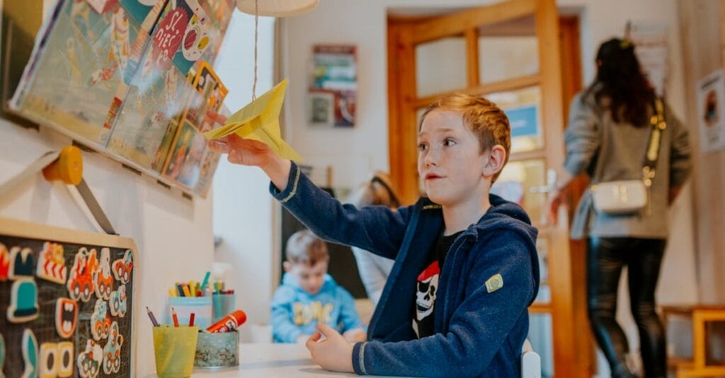 A young boy enjoying a creative activity with a paper airplane in a lively classroom setting.