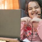 Smiling young girl with headset on a video call, studying online at home.