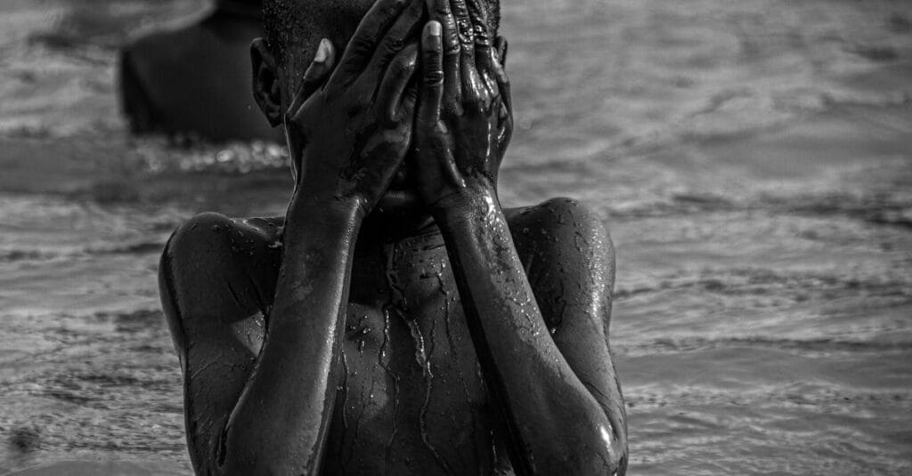 Emotive black and white photo of a child covering face while in water.