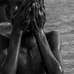 Emotive black and white photo of a child covering face while in water.