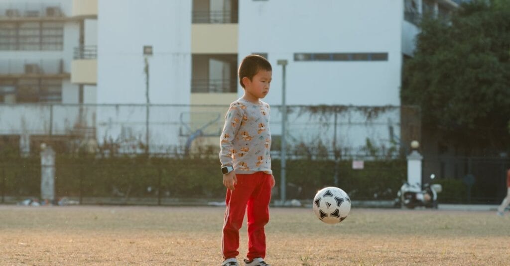 A young boy in a city park focuses on playing with a soccer ball during the day.