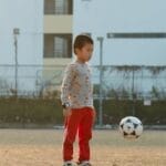 A young boy in a city park focuses on playing with a soccer ball during the day.