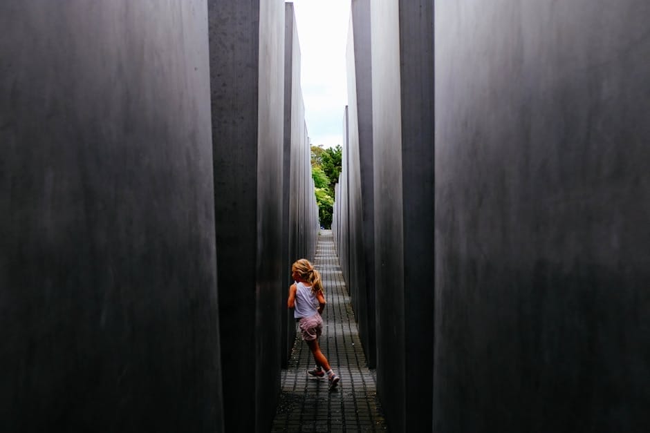 A young girl runs playfully through the narrow pathways of a modern concrete monument.